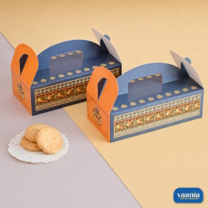 Two blue and orange Hamper Boxes with ethnic floral patterns sitting next to a small plate of cookies.