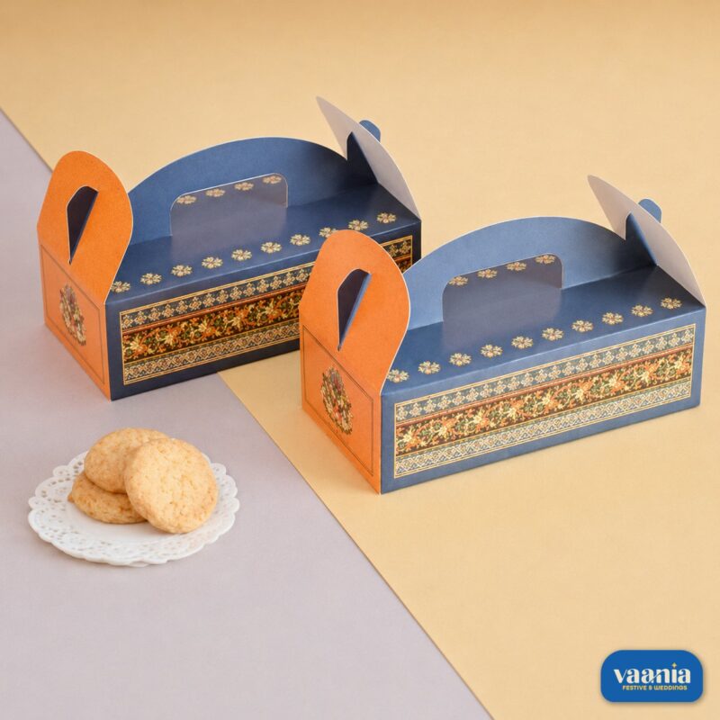 Two blue and orange Hamper Boxes with ethnic floral patterns sitting next to a small plate of cookies.
