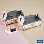 Two dark green Hamper Boxes with pink palace illustrations and die-cut handles next to gourmet chocolates.