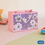 A purple and pink floral Gift Carry Bag with white rope handles sitting on a two-tone surface.
