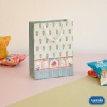 A decorative Gift Carry Bag with floral patterns and heritage arch illustrations sitting next to snack packets.