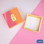 A pink and orange printed Sliding Box with Tray next to its empty golden inner tray on a split-tone background.