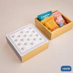 A luxury gold Sliding Box with Tray featuring a floral lid and filled with snacks alongside a closed matching box.