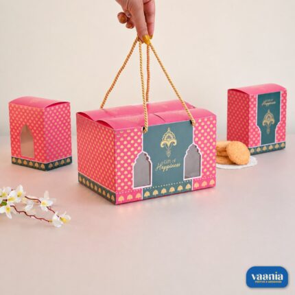 A hand holding a pink Hamper Bag Set with gold patterns and rope handles containing four boxes.