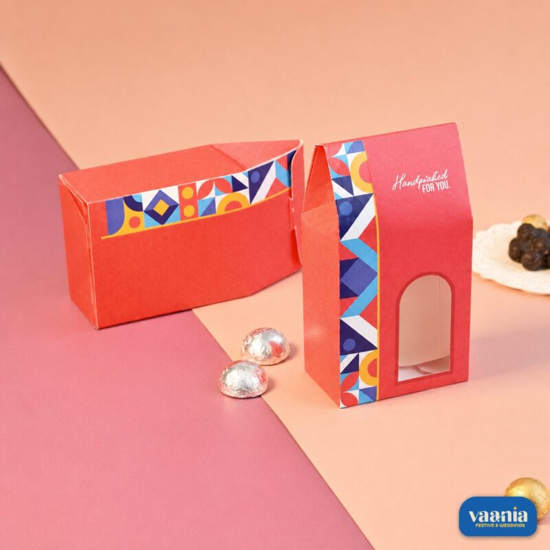 Two red Window Candy Boxes with geometric patterns and silver chocolates on a pink and peach background.