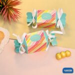 Two bright turquoise and striped candy-shaped Toffee Shape Boxes with white ribbons and gold chocolates nearby.