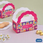 A pink and multicolored geometric print Hamper Bucket with scalloped handles next to cookies and chocolates.