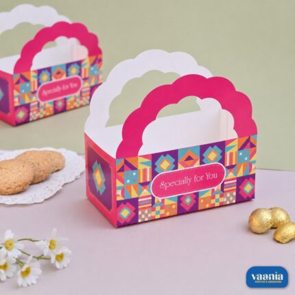 A pink and multicolored geometric print Hamper Bucket with scalloped handles next to cookies and chocolates.