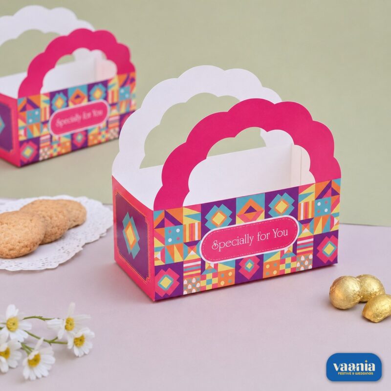A pink and multicolored geometric print Hamper Bucket with scalloped handles next to cookies and chocolates.