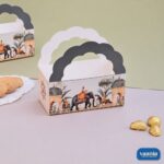 A decorative Hamper Bucket with royal Indian prints and scalloped handles sitting next to cookies and chocolates.