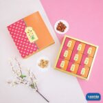 Top view of an orange and pink floral Sliding Box with nine smaller inner boxes beside decorative almonds and cashews.