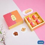 An ornate orange and pink Sliding Box with four inner containers next to almonds, cashews, and cookies.