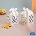 Two white and gold Hut Chocolate Boxes with lattice cutouts and satin ribbons filled with gold-wrapped chocolates.