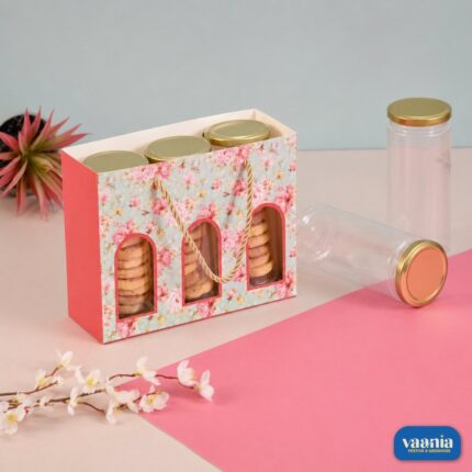 A floral pink Jar Hamper Bag holding three golden-capped jars filled with cookies on a pink background.