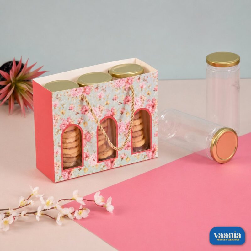 A floral pink Jar Hamper Bag holding three golden-capped jars filled with cookies on a pink background.
