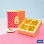 A pink and orange floral sliding box next to a gold 4-compartment tray with cashews on the side.