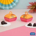 Two orange and pink Multi Purpose Boxes with peacock designs and heart-shaped chocolates on a pink table.