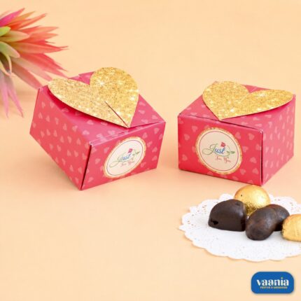 Two pink Heart Container Boxes with gold glitter heart lids and chocolates on a white doily.