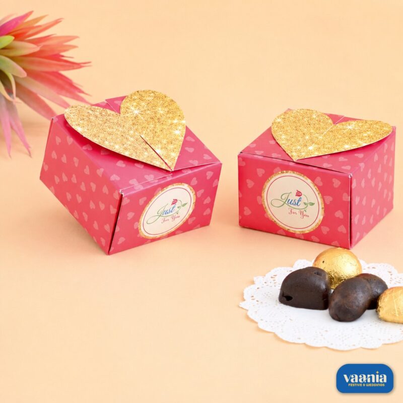 Two pink Heart Container Boxes with gold glitter heart lids and chocolates on a white doily.