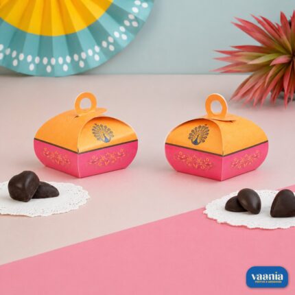 Two orange and pink Multi Purpose Boxes with peacock designs and heart-shaped chocolates on a pink table.