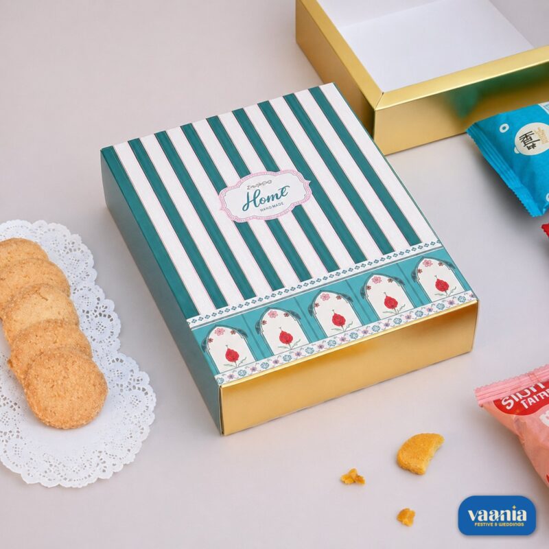 A decorative teal and gold Sliding Box with floral patterns next to butter cookies on a doily.