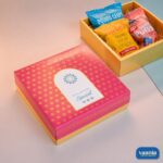 Top-Bottom Hamper featuring a pink floral lid and an open yellow base filled with assorted colorful snack packets.