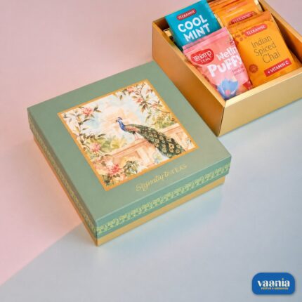 A luxury Top-Bottom Hamper with a peacock design lid next to an open gold box filled with colorful tea packets.