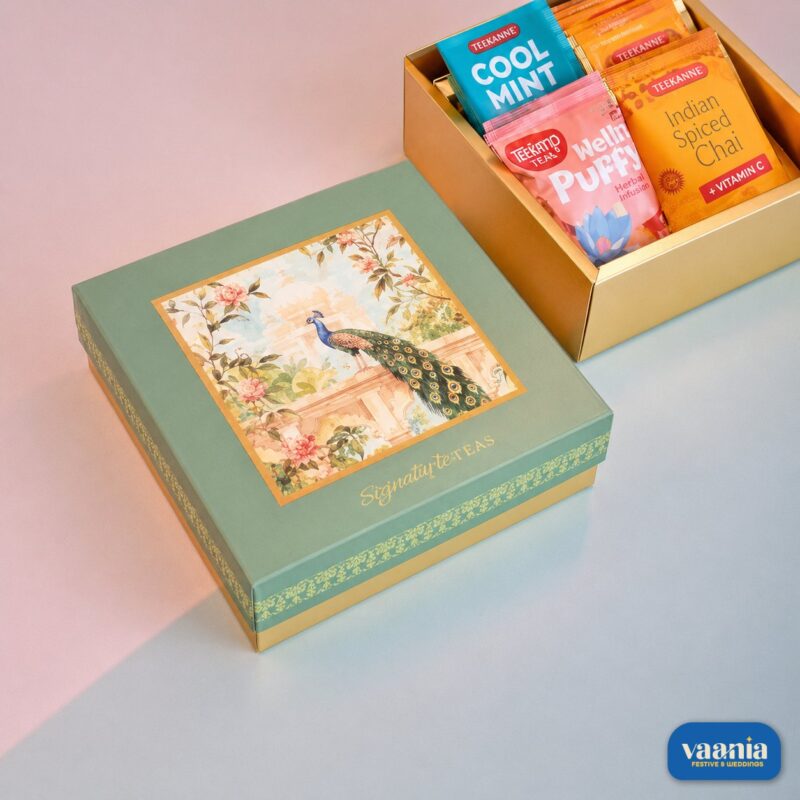 A luxury Top-Bottom Hamper with a peacock design lid next to an open gold box filled with colorful tea packets.