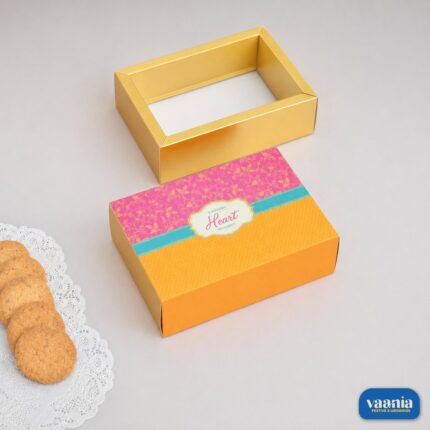 A decorative Sliding Box with a pink and yellow patterned cover next to an open gold-colored frame and cookies.
