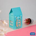 A turquoise Hut Hamper Box with white patterns and gold handles next to a small potted plant.