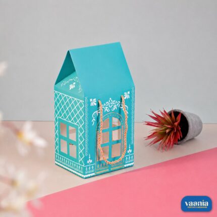 A turquoise Hut Hamper Box with white patterns and gold handles next to a small potted plant.