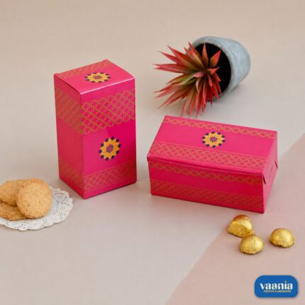 Two pink Vaania Multi Purpose Boxes with gold patterns shown with cookies and chocolates on a neutral background.