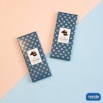 Two navy blue Premium Chocolate Bar Boxes with gold leaf patterns on a pink and blue background.